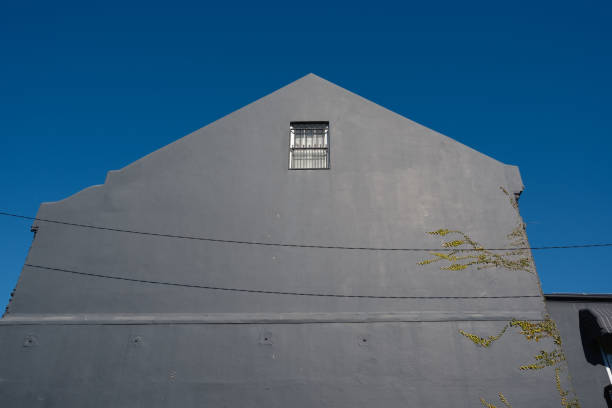 Top of a building with one window and deep blue sky above.