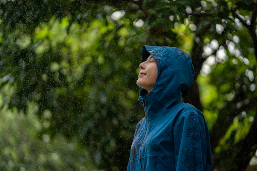 Portrait of a young woman standing happily in rain with her raincoat against purple background