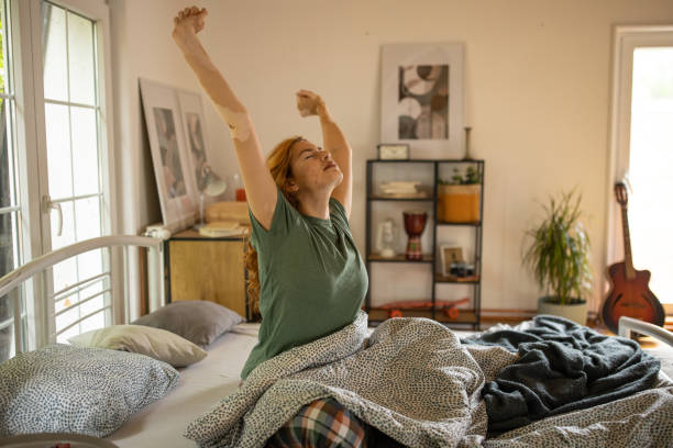 istock Young woman waking up and stretching in her bed 1555309952