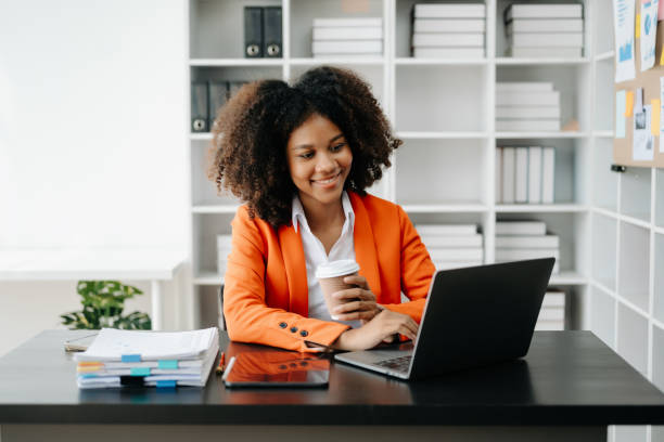 istock Young African woman typing on tablet and laptop while sitting at the working black table office 1555311034