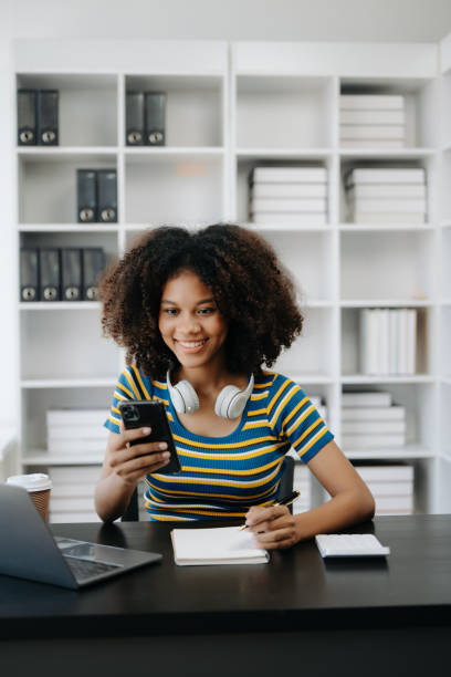 istock Beautiful African woman using laptop and tablet while sitting at her working place. Concentrated at work in home office 1555311554