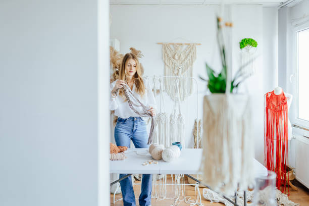 istock Adult attractive woman create working on an unfinished macrame piece, weaving ropes. Creative craftswoman in workshop space. Weaving art hobby concept. 1555331322
