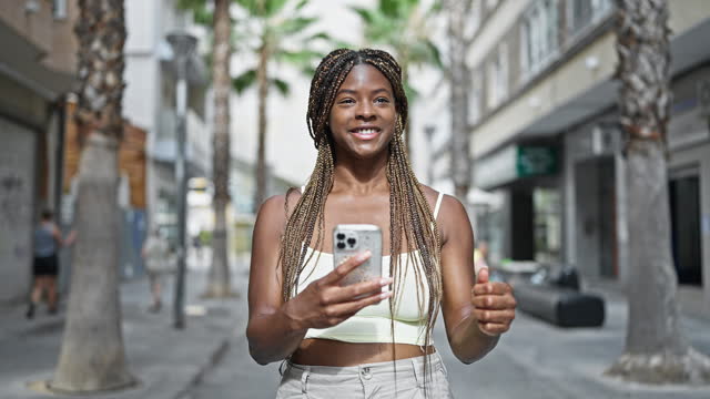 African american woman using smartphone with winner gesture at street