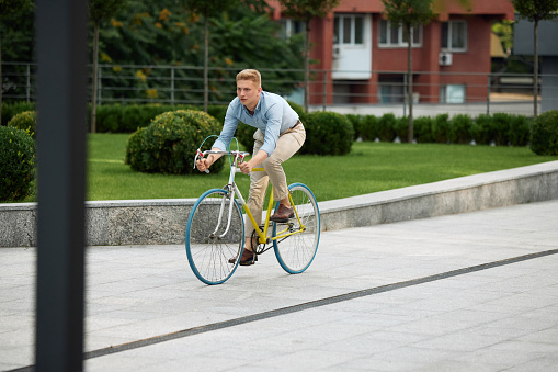 Stylish young man, office worker, employee riding to work on bike along the street on warm summer day. Urban background. Concept of business, active lifestyle, fashion, youth, ecology