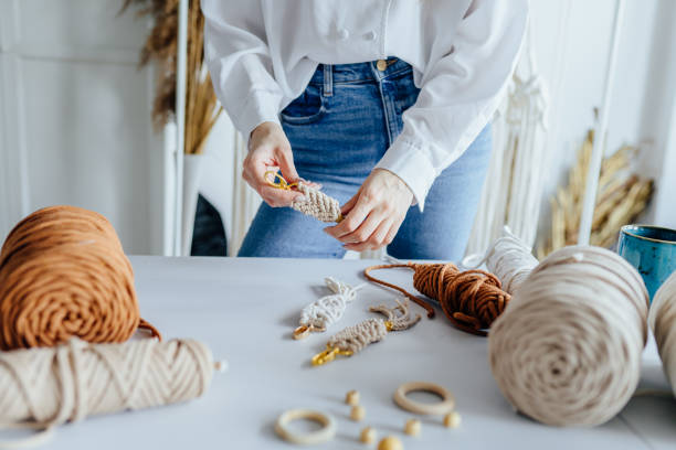Hand of unrecognizable woman when she is making macrame. Natural cotton threads. Handmade macrame in work process.