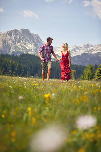 Beautiful young couple holding hands and running on green meadow. Fun, togetherness, lifestyle, nature concept.