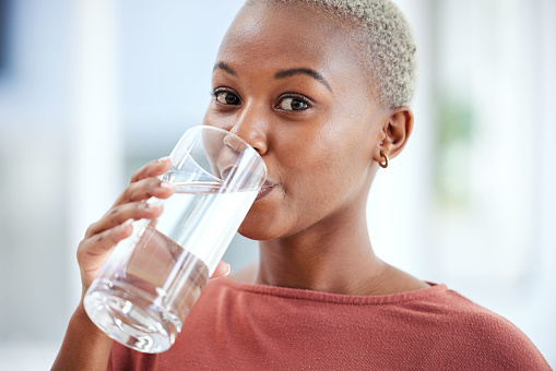 Health, glass and portrait of a woman drinking water for hydration, wellness and liquid diet. Healthy, h2o and headshot of young African female person enjoying a cold beverage or drink at her home.