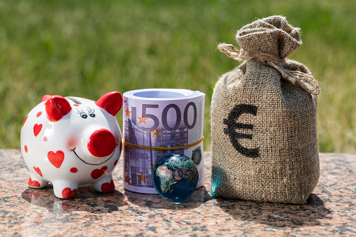 A rolled bundle of 500 euro banknotes, piggy bank, money bag  and a glass globe