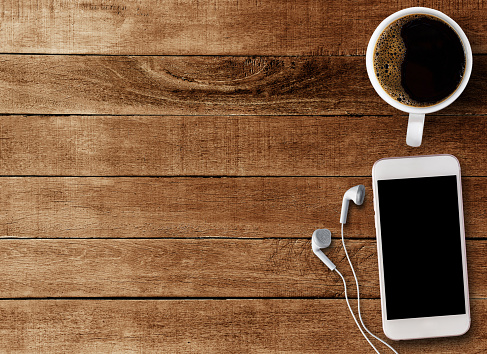 Top view Smart phone and earphone with cup of coffee on old wooden background with copy space.