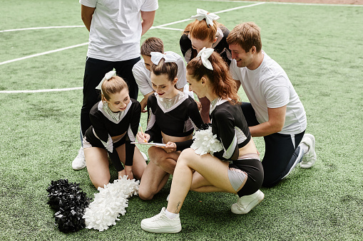 Girl from cheerleader team writing on paper to plan their performance during sport competition outdoors