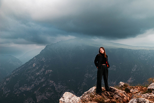 A woman wearing dark clothes standing at the top of Tara river Canyon in Montenegro, with a  dramatic sky on background