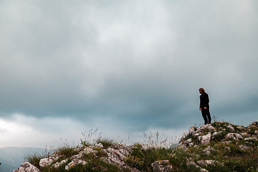 A man wearing dark clothes standing at the top of Tara river Canyon in Montenegro, with a  dramatic sky on background