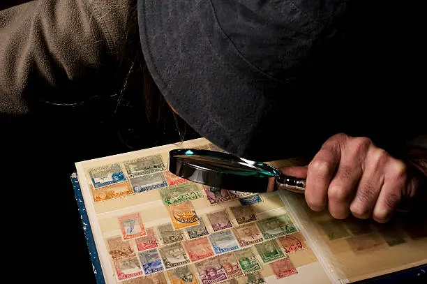 A postage stamp collector watching his collection of stamps with a magnifying glass