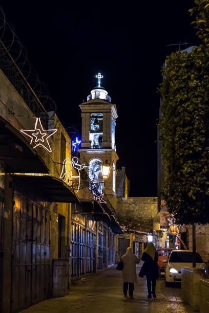 Vertical night view of two women walking on Milk Grotto St with the bell tower of the Church of the Nativity (or Basilica of the Nativity) in the background in Bethlehem