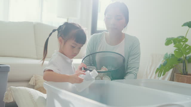 Closeup of young Asian family mom teaching kid how to recycle help girl aware environmental importance in living room at home. Family happy moment concept.