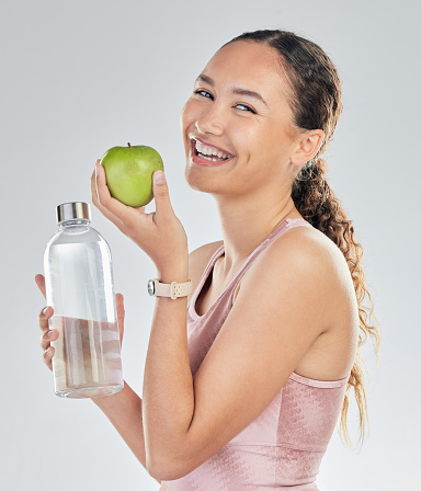 Portrait, woman and water bottle with apple in studio for diet of healthy food, nutrition and detox for weightloss. Happy female fitness model, hydration and fruit to lose weight on white background