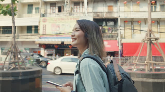Young Asian woman backpacker using a mobile phone on street in urban city. Holiday vacation trip concept.