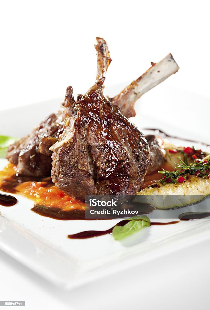 Cooked lamb chops with vegetables on a white plate Roasted Lamb Chops on Tomato Sauce Garnished with Vegetables and Basil Basil Stock Photo