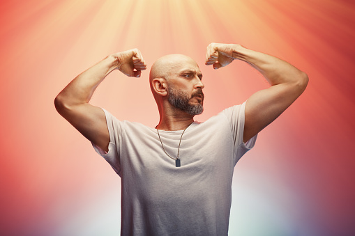 Man flexing his arms muscles and biceps showing his strength and male power, colorful background