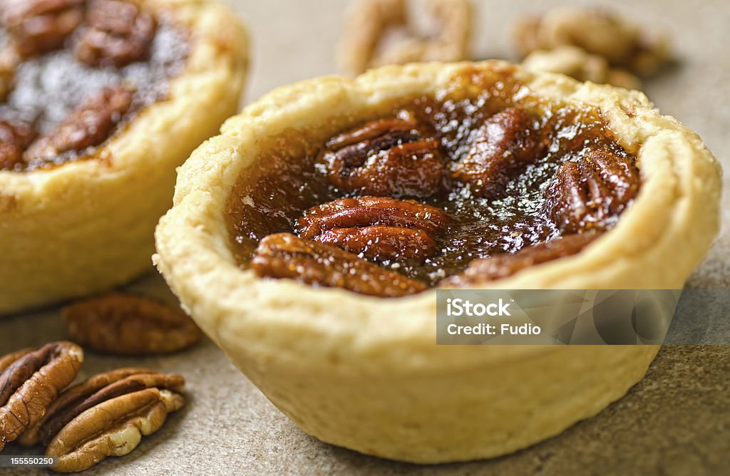 Close-up photograph of pecan tartlets and pecan nuts Two pecan tarts with pecans set against a simple background. Tart - Dessert Stock Photo