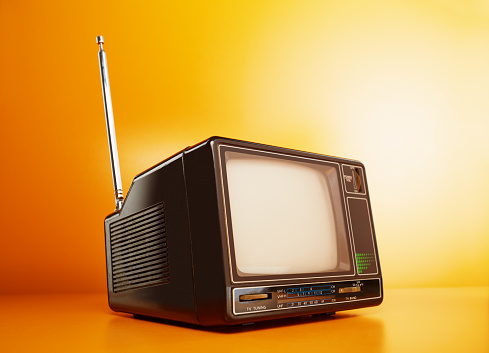 Old vintage television on orange. Retro portable tv receiver with antenna on orange background