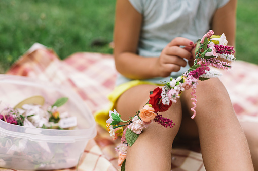 Close up details of a girl making flower wreath sitting on a picnic in nature
