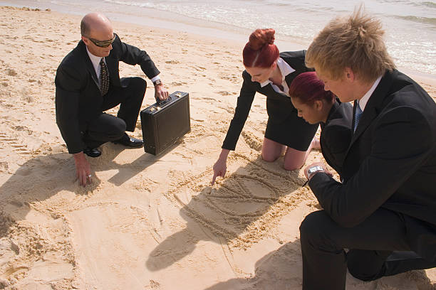A Businesswoman Drawing a Pie-chart in the sand at the beach with team members looking on