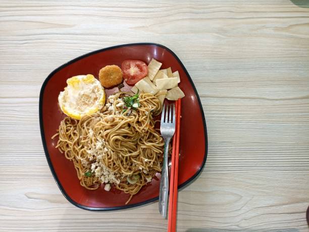istock Spicy Fried Instant Noodles with Topping Dumplings, eggs, tomatoes on a red plate 1555603385