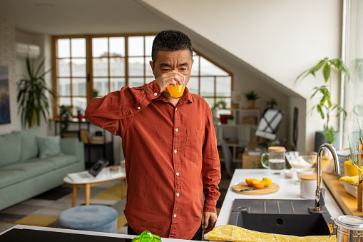 Mature Chinese man drinking fresh orange juice in the kitchen of his apartment