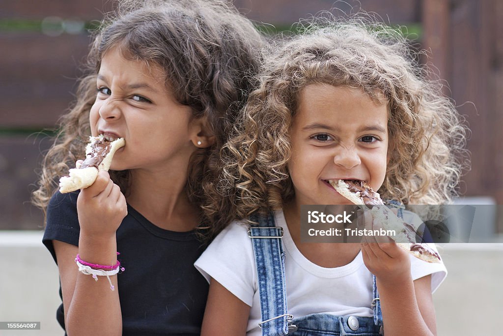 Sisters eating Sisters crunching heartily into a slice of bread with chocolate Beautiful People Stock Photo