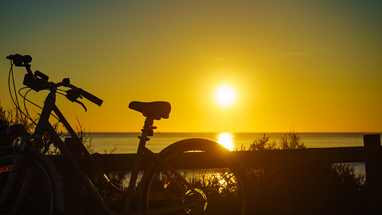 Bicycle outdoor parked on beach, evening time, sunset sky. Holidays, sport and recreation.