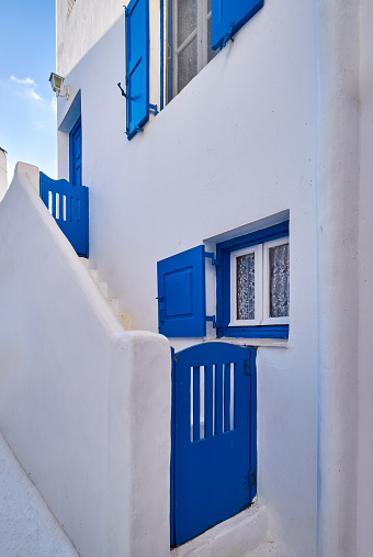 Traditional Greek house on Cyclades or Aegean islands. Whitewashed walls and dark blue doors, storm shutters and window frames. Colors of Greece. Entrance, stairs. Authentic decoration, Mediterranean style.