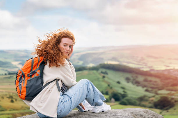 frau in jacke und rucksack erreicht das ziel und auf dem gipfel des berges bei sonnenuntergang. travel lifestyle konzept der nationalpark peak district in england - toll free audio stock-fotos und bilder