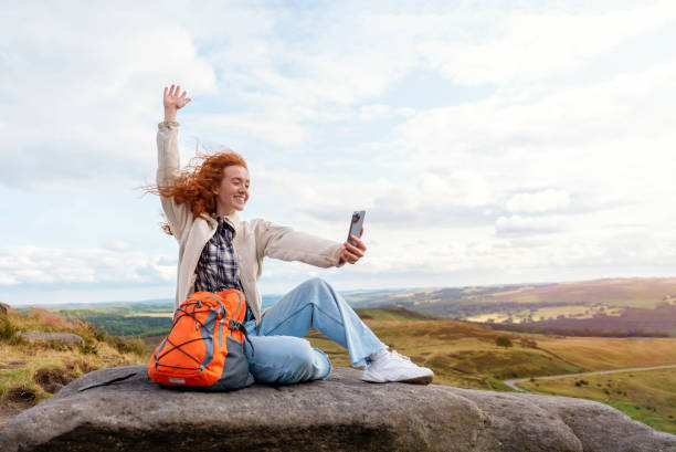 glückliche frau in jacke und rucksack, die das ziel erreicht, auf dem gipfel des berges und fotos per telefon bei sonnenuntergang macht. travel lifestyle konzept der nationalpark peak district in england - toll free audio stock-fotos und bilder