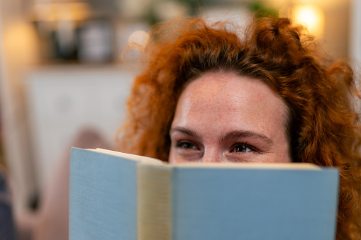 Close up of a woman hiding behind the book.