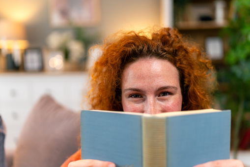 Portrait of a cheeky woman holding a book at home during the day.