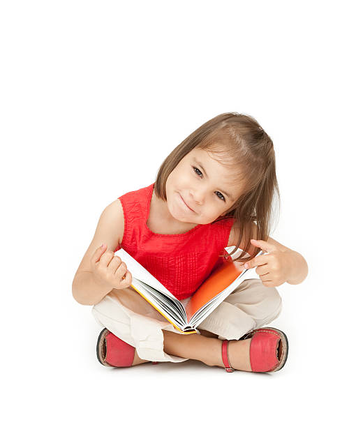 little girl reading a book little girl reading a book isolated on white kid sitting cross legged stock pictures, royalty-free photos & images