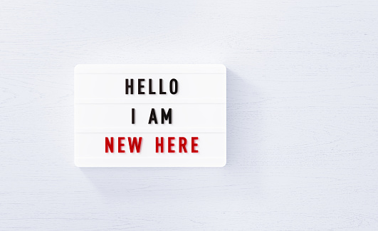Hello I am new here written white lightbox on white wood background. Horizontal composition with copy space.