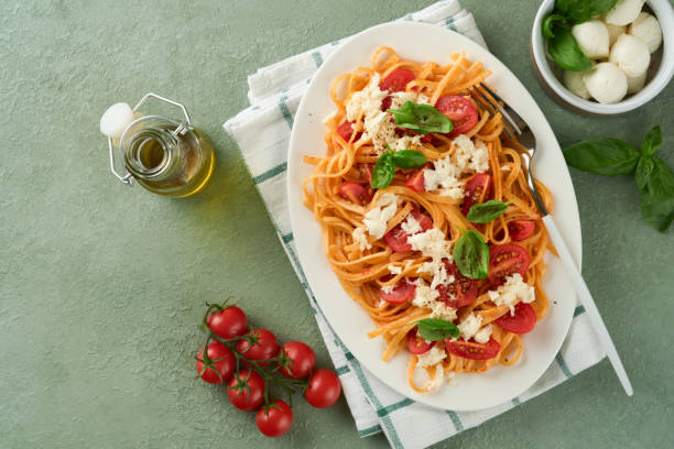 salat-caprese oder pasta-spaghetti gebrochen mit basilikum und mozzarella ala caprese auf weißem teller auf grünem rustikalem holzhintergrund. traditionelle italienische küche. italienisches food-konzept. draufsicht. rezept. - caprese salad antipasto wine mozzarella stock-fotos und bilder