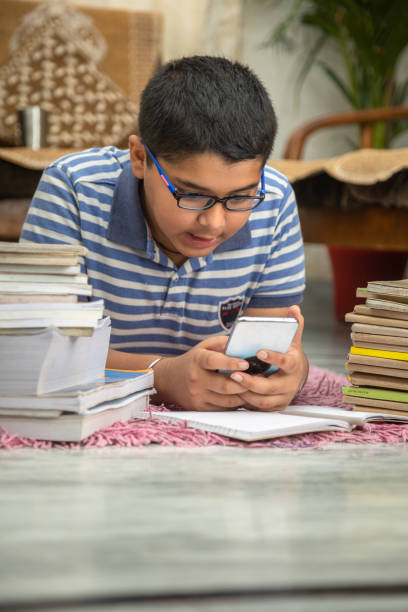 istock Boy lying down on floor with bunch of books and using mobile phone 1555716721