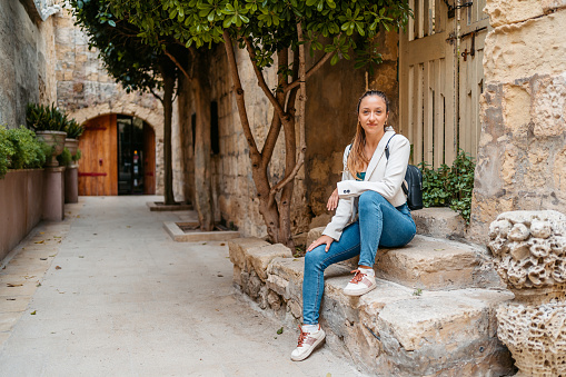 Portrait of a beautiful young woman sitting on the steps in Mdina in Malta.