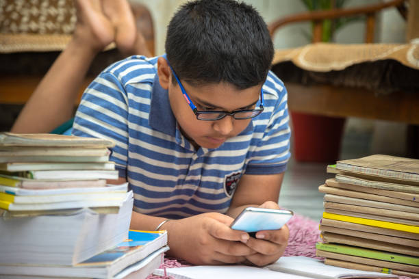 istock Boy lying down on floor with bunch of books and using mobile phone 1555720466