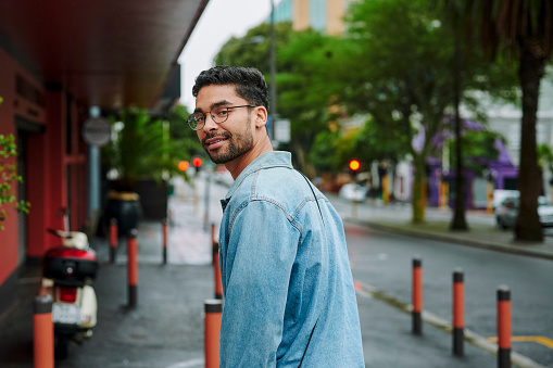 Portrait of a confident young man looking over his shoulder and smiling while walking along a city sidewalk