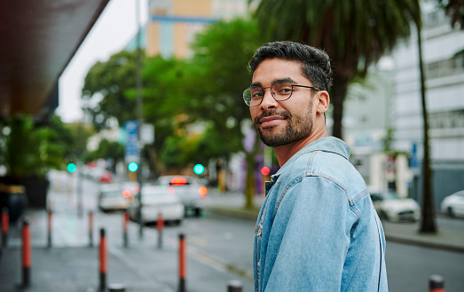 Portrait of a smiling young man looking over his shoulder while walking along a sidewalk in the city