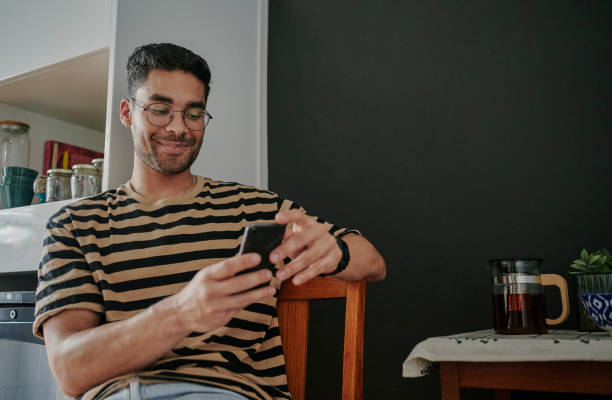 istock Smiling young man scrolling through his smart phone in his kitchen 1555725248