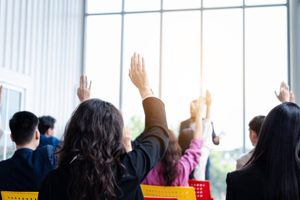 istock Business person raising hand during seminar. Hand up in conference asking to answer a question in business meeting room and seminar class. 1555729582