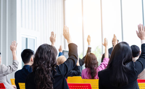 istock Business person raising hand during seminar. Hand up in conference asking to answer a question in business meeting room and seminar class. 1555729587