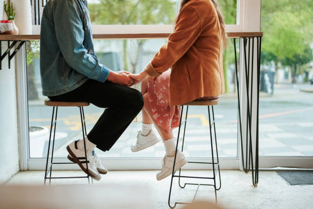 Young couple sitting in a cafe and holding hands during a date Unrecognizable young couple holding hands while sitting together by a window in a cafe during a date flirting stock pictures, royalty-free photos & images