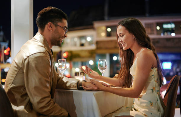 istock Smiling young couple holding hands together during an evening dinner date 1555729944