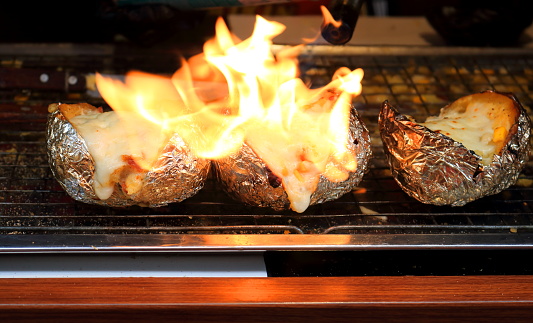 Potato and cheese topping on metal grate in row are fire burning cheese.